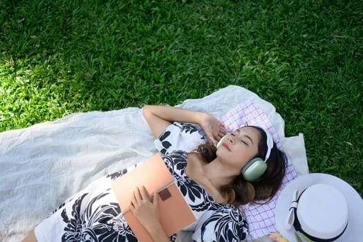 Beautiful young woman taking a nap on picnic blanket with with open book in her hand.