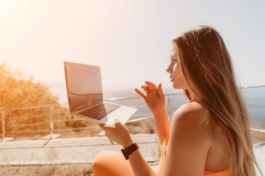 Digital nomad, Business woman working on laptop by the sea. Pretty lady typing on computer by the sea at sunset, makes a business transaction online from a distance. Freelance, remote work on vacation