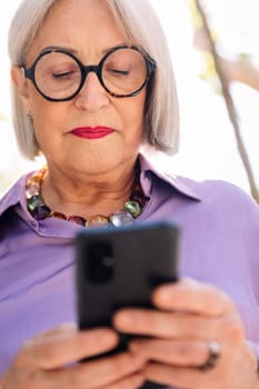 close up portrait of a senior woman using mobile phone on the street, concept of technology and elderly people leisure
