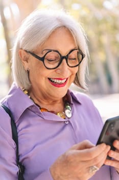 portrait of a senior woman smiling happy using mobile phone outdoors, concept of technology and elderly people leisure