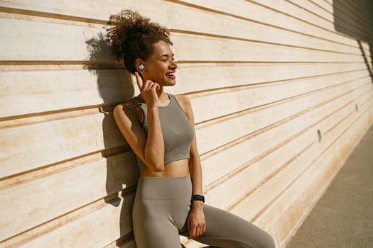 Smiling woman in sportswear have a rest after workout outside standing on wall background