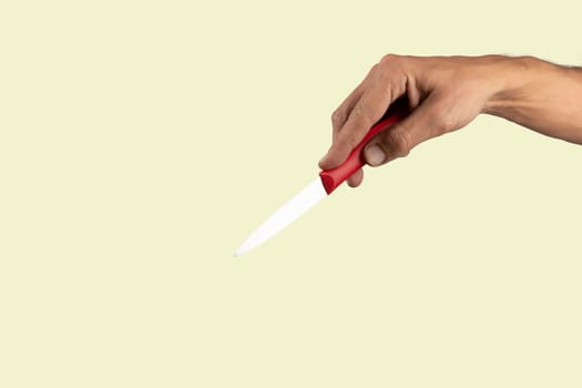 Black male hand holding a red cooking knife isolated on light green background. High quality photo