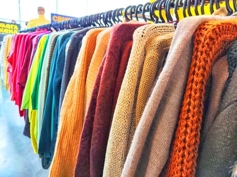 Colorful Assortment of Knitted Sweaters on Display in Bright Clothing Store. Variety of colorful sweaters hanging on a rack in a shop