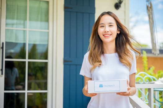 Online delivery medical. Portrait of Asian young woman smile hold medication box first aid shipment received from pharmacy hospital delivery at home patient, Buy online clinic retail Rx drug store