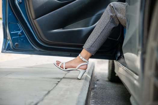 A businesswoman symbol of style and success is seated in her luxury car. Her elegant leg encased in high heels opens door marking her departure from world of glamour and entering realm of business.