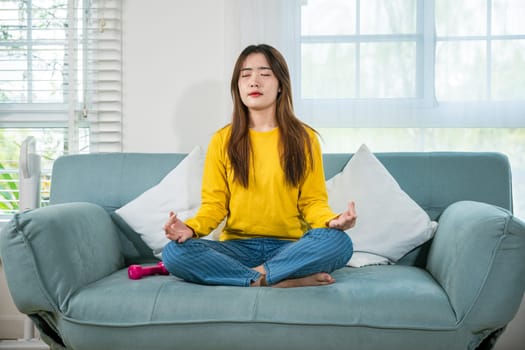 Young woman practise yoga and meditation in lotus position, mindfulness lifestyle, Asian female sits on sofa at home and chilling with couch lotus pose eyes closed, happy relaxation leisure people