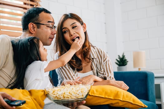 In their cozy house a smiling young family gathers on sofa watching TV with popcorn. father mother son daughter and schoolgirl share laughter joy and relaxation epitomizing family togetherness.