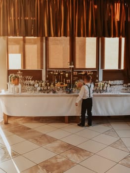 Boy stand eating near catering wedding buffet for events. Beautifully decorated catering banquet table food snacks and appetizers with sandwich. decorated catering banquet table burgers profiteroles