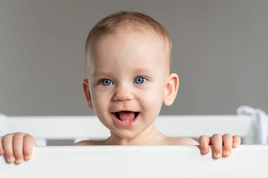 The cheerful face of a baby slyly peeking out of the crib.