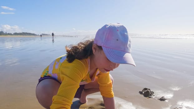 Little girl joyfully clamming on Pismo Beach, bundled up for the winter chill as she explores the sands for seashells and clams.