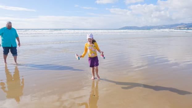 Father and daughter enjoy a leisurely winter walk along the picturesque Pismo Beach, sharing quality time together amid the serene backdrop of gently crashing waves.