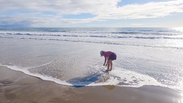 A little girl joyfully plays on the vast, empty sands of El Capitan State Beach in California during winter.