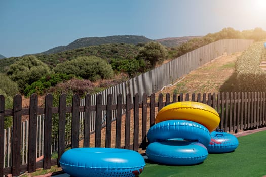 Blue and yellow inflatable wheels against background of wooden fence and nature on sunny day