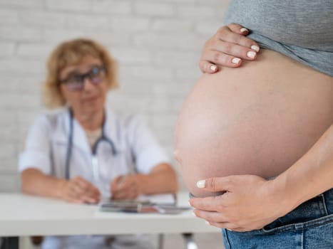 Doctor obstetrician gynecologist at his desk in the background. Close-up of a pregnant woman's belly
