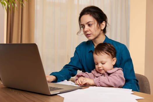 beautiful businesswoman working on laptop with her little child girl at home