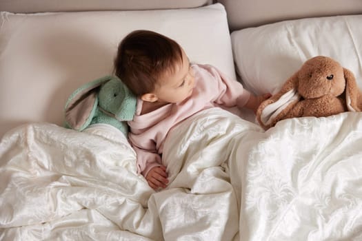 cute little child with fluffy toy bunny in white bed