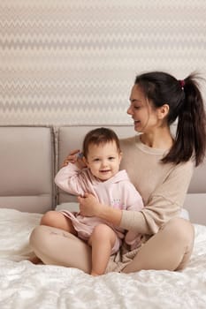 attractive mother is combing her cute little daughter hair on bed