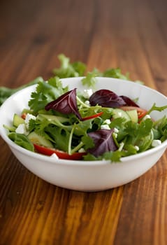 spring salad with tomatoes, cucumbers, lettuce leaves and herbs in a bowl on a wooden table. AI generated image.