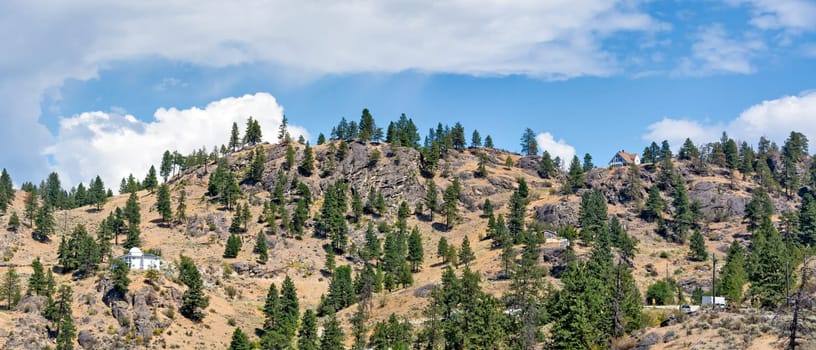 Mountain landscape with residential houses on hot summer day with cloudy sky background