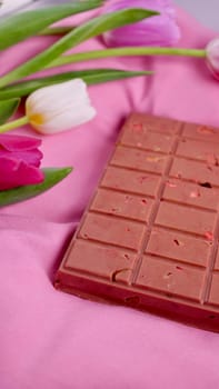 A bar of pink ruby chocolate with sublimated freeze-dried strawberries and almonds and spring tulip flowers . A dessert based on berries and nuts for International Women's Day, March 8, mother's day