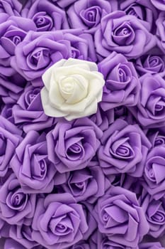 vertical image top view of background of purple or lilac flowers and one white flower. artificial flowers. Artificial purple or lilac roses and one white rose from foamiran. soft focus. flat lay