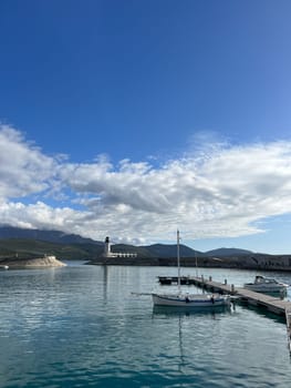 Boats moored at the pier against the backdrop of a lighthouse at the foot of the mountains. High quality photo