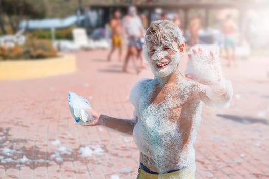 Happy smiling boy with foam on whole body at a foam party or holiday on a sunny hot summer day.