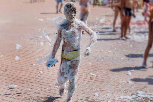 Happy boy with foam on whole body at a foam party or holiday on a sunny hot summer day.