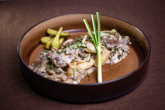 Indulge in a flavorful beef stew with mushrooms, sour cream, and tangy pickles on the side, a comforting and satisfying meal to savor.