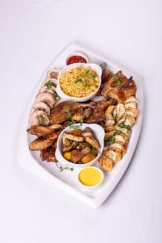 Assorted roasted meats, colorful vegetables, and golden potatoes garnished with fresh parsley and savory sauces on a white platter.