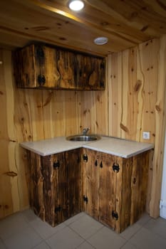 Rustic wooden kitchen corner cabinet with sink, doors, wood grain pattern, white marble countertop, knotty pine walls, sink.