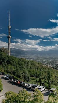 A vibrant cityscape with towering mountains and a distinct telecommunications tower, captured from an aerial perspective.