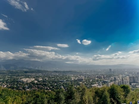 A beautiful cityscape with mountains in the background. The sky is blue with white clouds and the sun is shining.