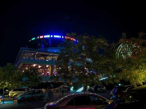 Illuminated modern glass and steel structure with vibrant night sky and colorful Ferris wheel in the background.