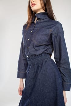 A young woman in a blue denim shirt dress with a collar and long sleeves. Fitted at the waist with a stretchy waistband.