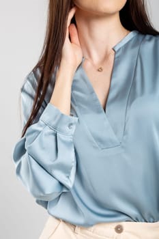 Young woman in blue satin blouse with plunging neckline, long sleeves, and smile. Brown hair, elegant look.