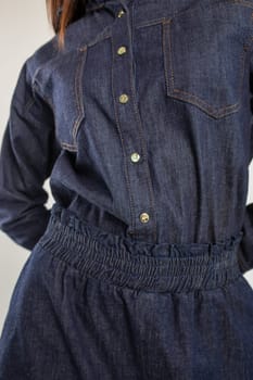 A young woman in a blue denim shirt dress with a collar and long sleeves. Fitted at the waist with a stretchy waistband.