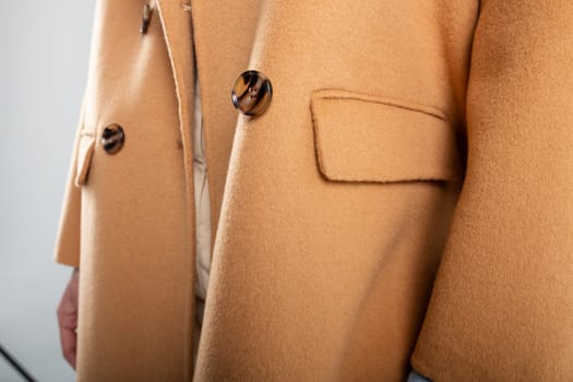 Stylish young woman in warm brown coat with large buttons. Posing near white wall. Copy space for text or advertisment.