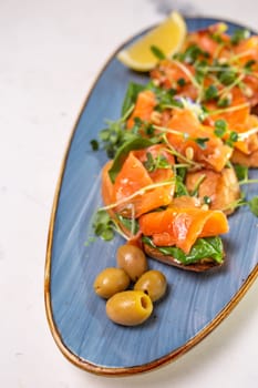 salmon with lemon, olives and microgreens on a blue plate on the table.