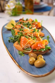 salmon with lemon, olives and microgreens on a blue plate on the table.