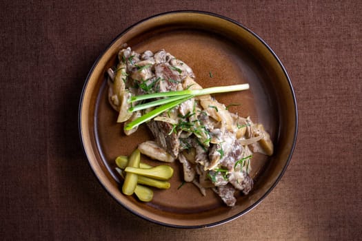 Indulge in a flavorful beef stew with mushrooms, sour cream, and tangy pickles on the side, a comforting and satisfying meal to savor.