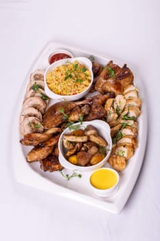 Assorted roasted meats, colorful vegetables, and golden potatoes garnished with fresh parsley and savory sauces on a white platter.