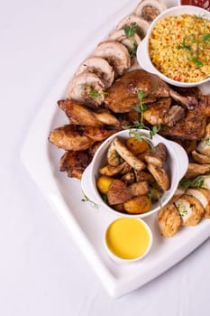 Assorted roasted meats, colorful vegetables, and golden potatoes garnished with fresh parsley and savory sauces on a white platter.