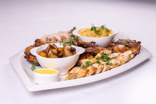 Assorted roasted meats, colorful vegetables, and golden potatoes garnished with fresh parsley and savory sauces on a white platter.