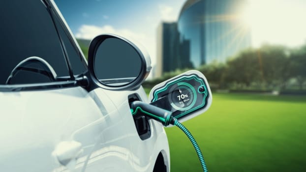 EV car plug in with charging station to recharge electricity from EV charger display battery status hologram in green park as futuristic eco lifestyle in city and utilization of clean energy. Peruse