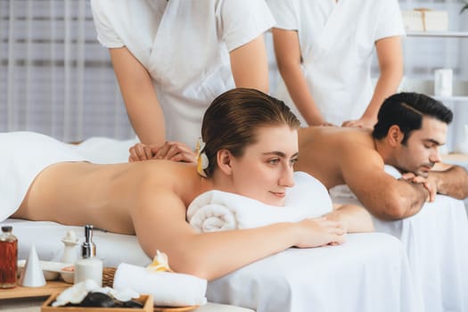 Caucasian couple customer enjoying relaxing anti-stress spa massage and pampering with beauty skin recreation leisure in day light ambient salon spa at luxury resort or hotel. Quiescent