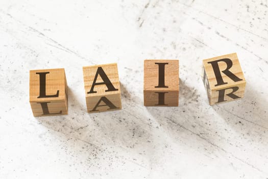 Four wooden cubes with letters LAIR (meaning Listen Acknowledge Identify Reverse) on white working board.