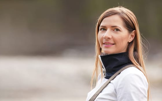 Portrait of young woman in white sport jacket, blurred horizon (river shore) in background, space for text left side