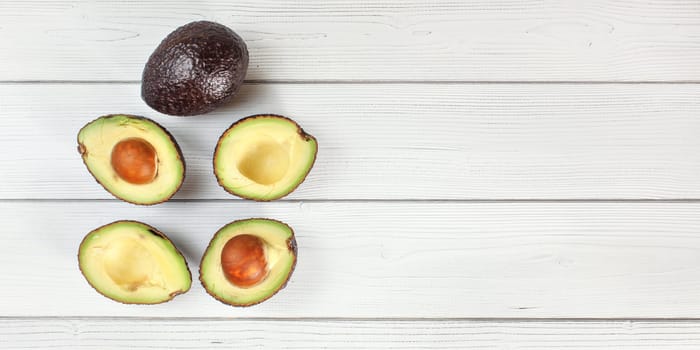 Ripe avocado halves and one whole fruit arranged on white boards desk, view from above - wide photo with space for text right side