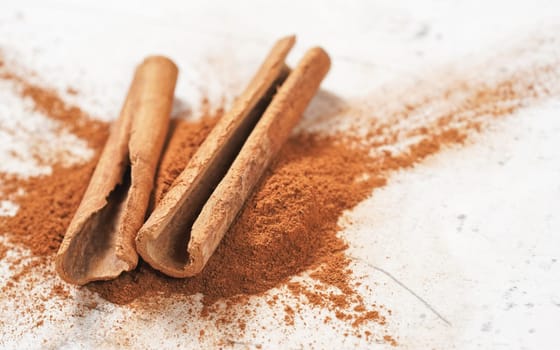 Two cinnamon sticks in small pile of grounded bark, on white stone like board